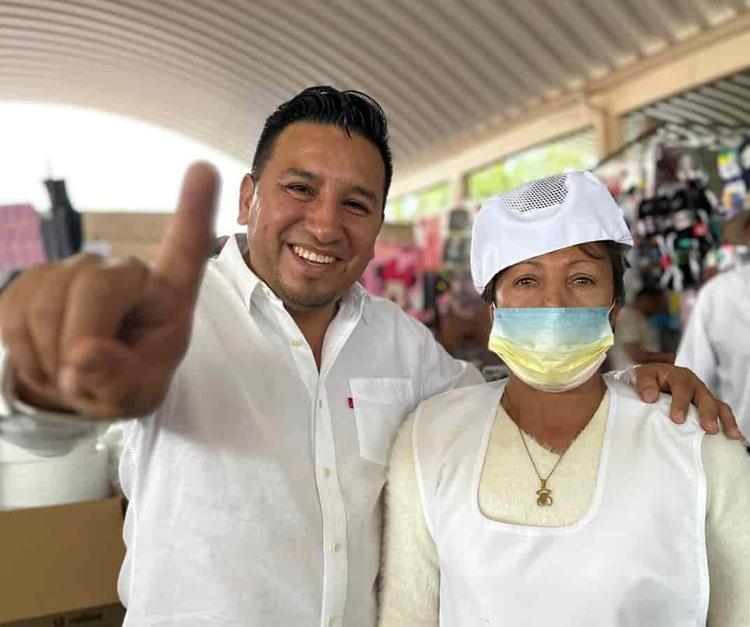 Paco realizando el símbolo de campaña en el mercado municipal junto a una señora